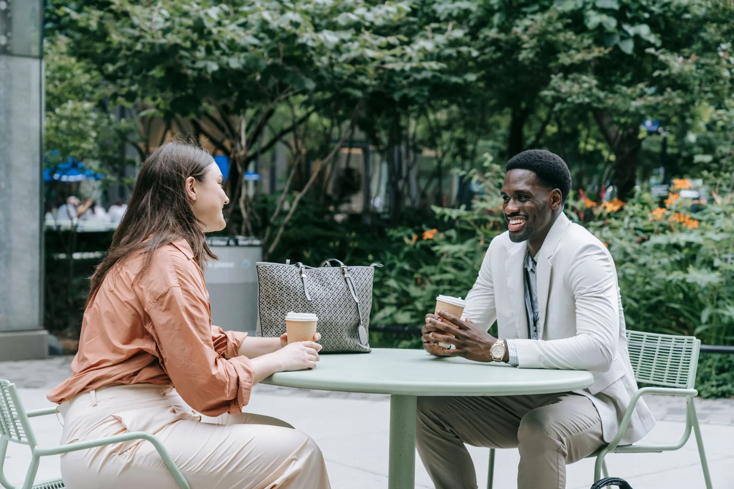 Two adults talking over coffee at an outdoor table. · Illustrative stock photo