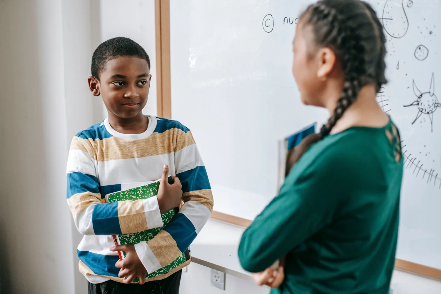 Children discussing schoolwork beside a classroom whiteboard. · Illustrative stock photo