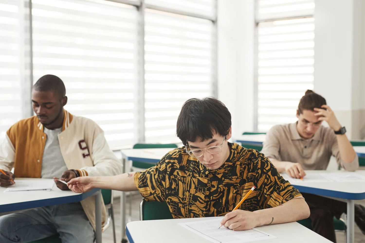 Students concentrating on a written exam in a classroom. · Illustrative stock photo
