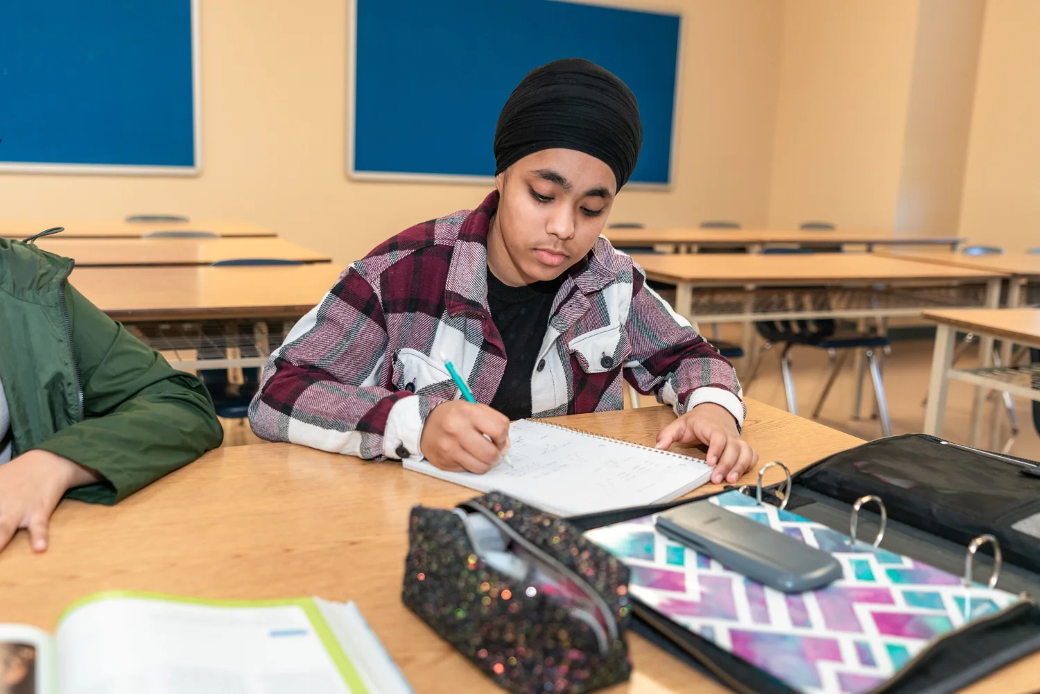 A teenage student writing in a notebook at a classroom desk. · Illustrative stock photo